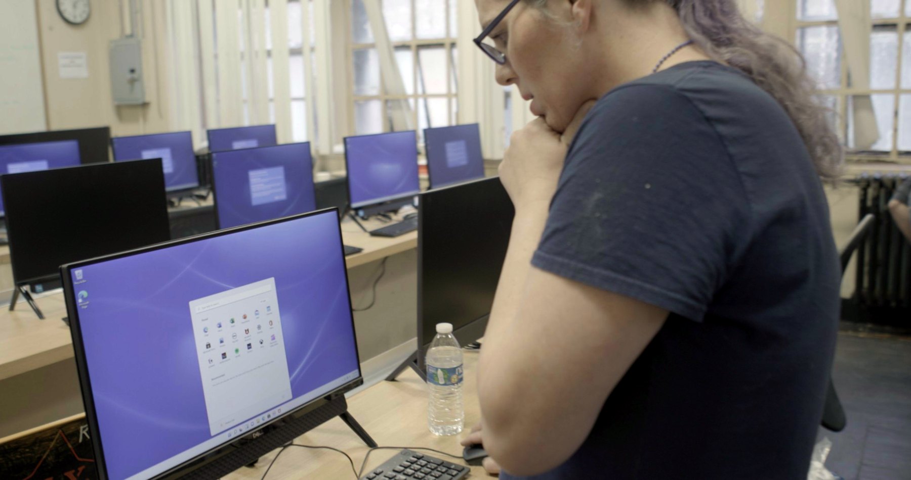 Jessica Hicklin looking at a monitor in a long room of new computers during a lab installation.